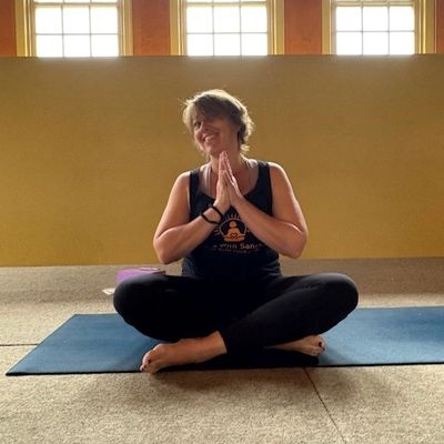 Woman sitting cross-legged on a yoga mat, hands in prayer position, smiling peacefully.