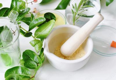 Mortar and pestle with powder surrounded by green leaves and glass containers.