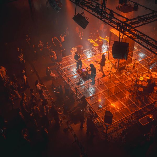 A band performing on a lit stage with an audience watching.