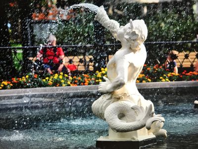 White statue of a mermaid spouting water in a fountain.