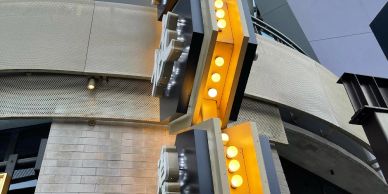 Vertical view of a modern building exterior with illuminated signage and architectural details.