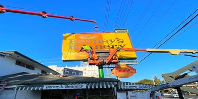 Workers install a Barney's Brewery sign using cranes.