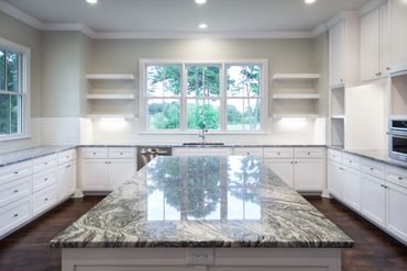 A kitchen with marble countertops on all sides and two windows