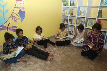 Children sitting on carpet reading books in a cozy room.