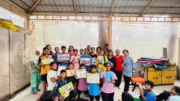 Group of children and adults holding colorful drawings inside a classroom.