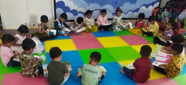 Children sitting in a circle on colorful mats, reading books.
