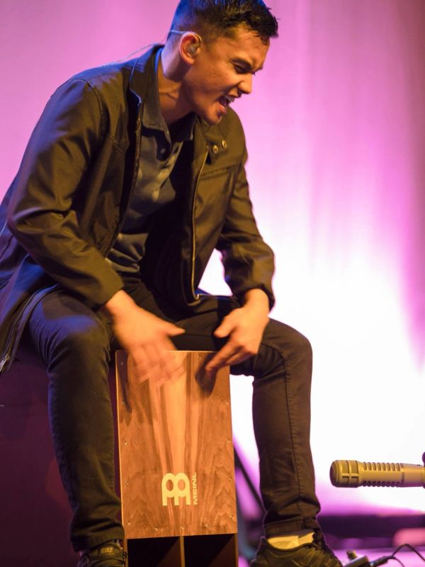Man energetically playing a cajón drum on stage.