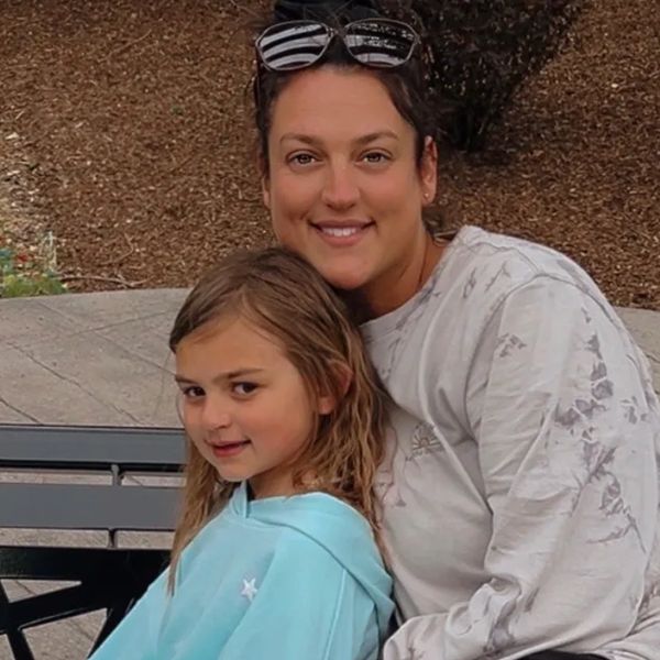 A smiling woman and young girl sitting together outdoors.