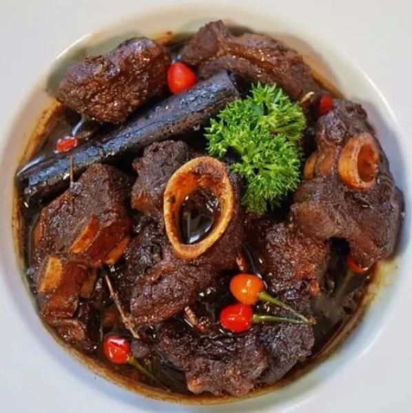 Plate of slowly simmered pepperpot, garnished with parsley and red wiri wiri peppers.
