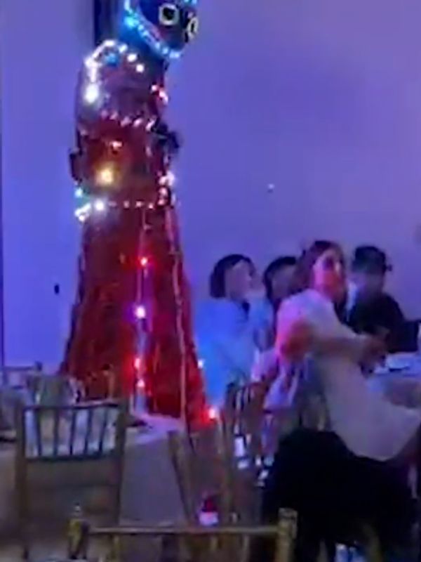 Tall figure on stilts adorned with colorful lights at an indoor event.