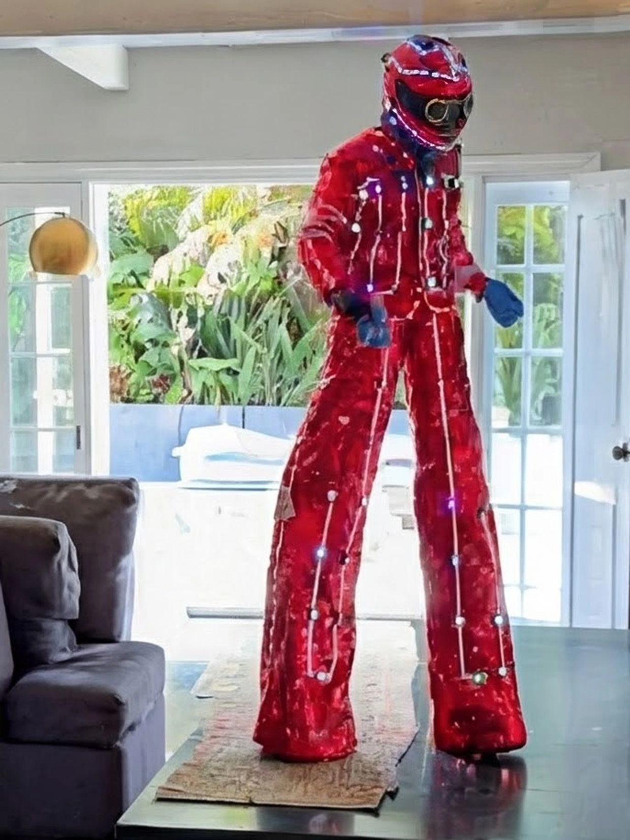Person in a red illuminated costume with stilts inside a living room.