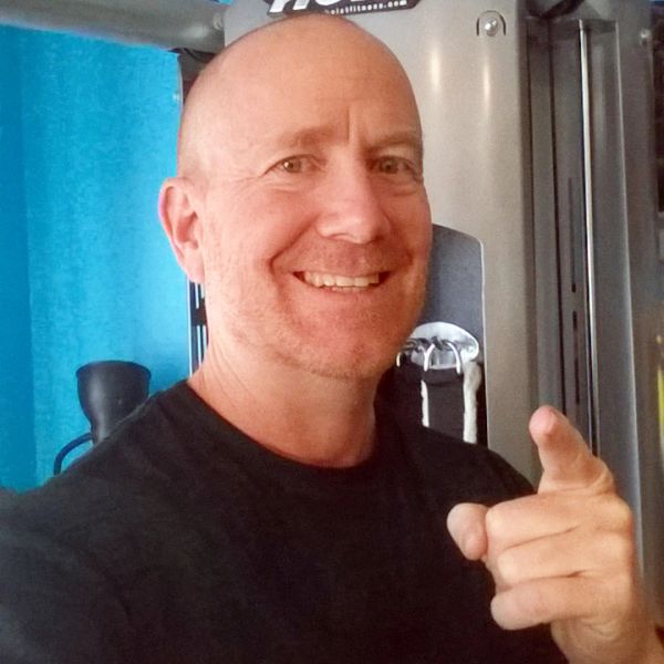 Smiling bald man pointing at the camera in a gym setting.
