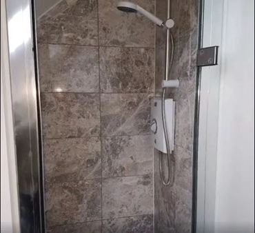 Modern shower stall with stone tiles and a mounted showerhead.
