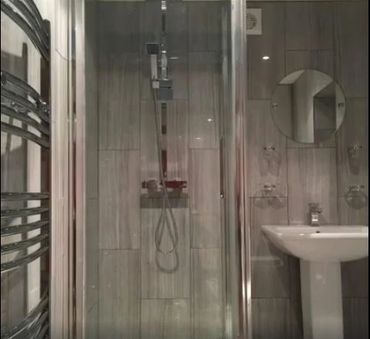 Modern bathroom with glass shower, pedestal sink, and round mirror.