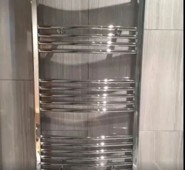 Shiny chrome towel radiator mounted on a tiled wall.
