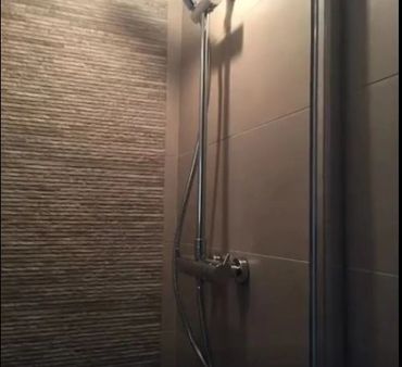 Modern shower setup with textured and smooth tile walls.
