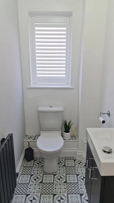 A modern bathroom with patterned tiles and a white toilet beneath a shuttered window.