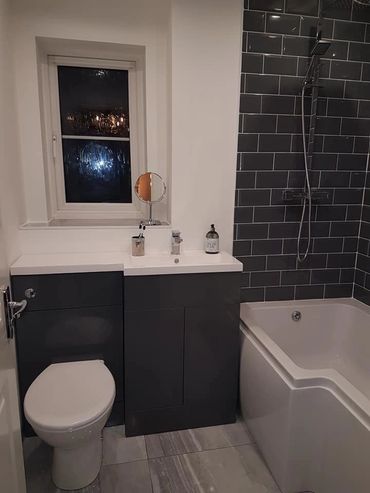 Modern bathroom with dark tiles, white bathtub, and compact vanity unit.