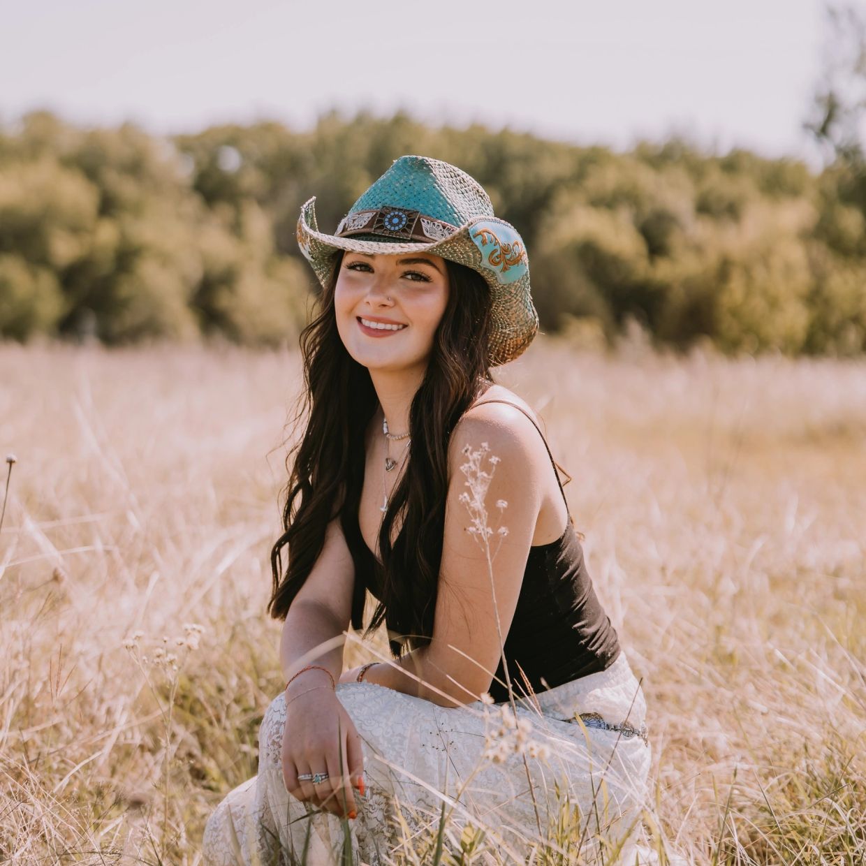 A young woman in a cowboy hat sitting in a field.