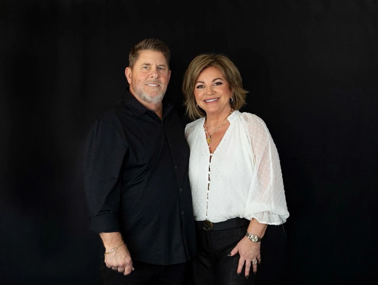 Smiling couple posing against a black background, dressed in black and white.