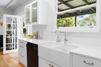Bright white kitchen with farmhouse sink and open door.