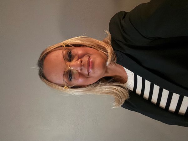 Smiling woman with blonde hair wearing glasses and a black blazer.