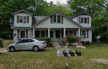 A two-story white house with three dormer windows and a parked silver car in front.
