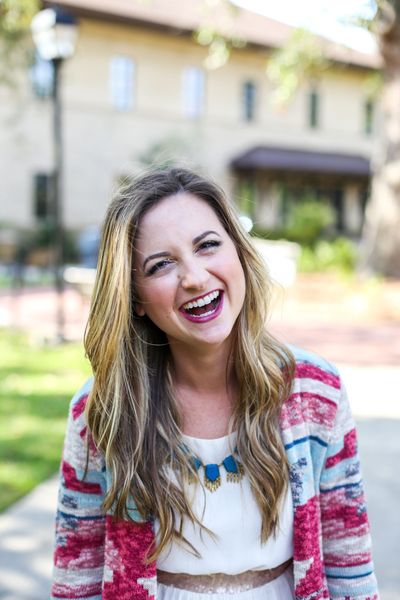 Picture of a woman with long, wavy hair and bright pink lipstick. She's laughing and wearing a cream