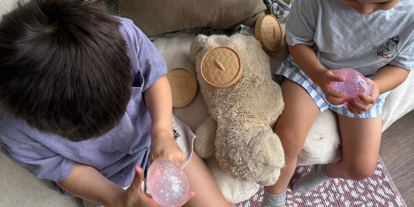 Two children holding translucent gel balls near a teddy bear.