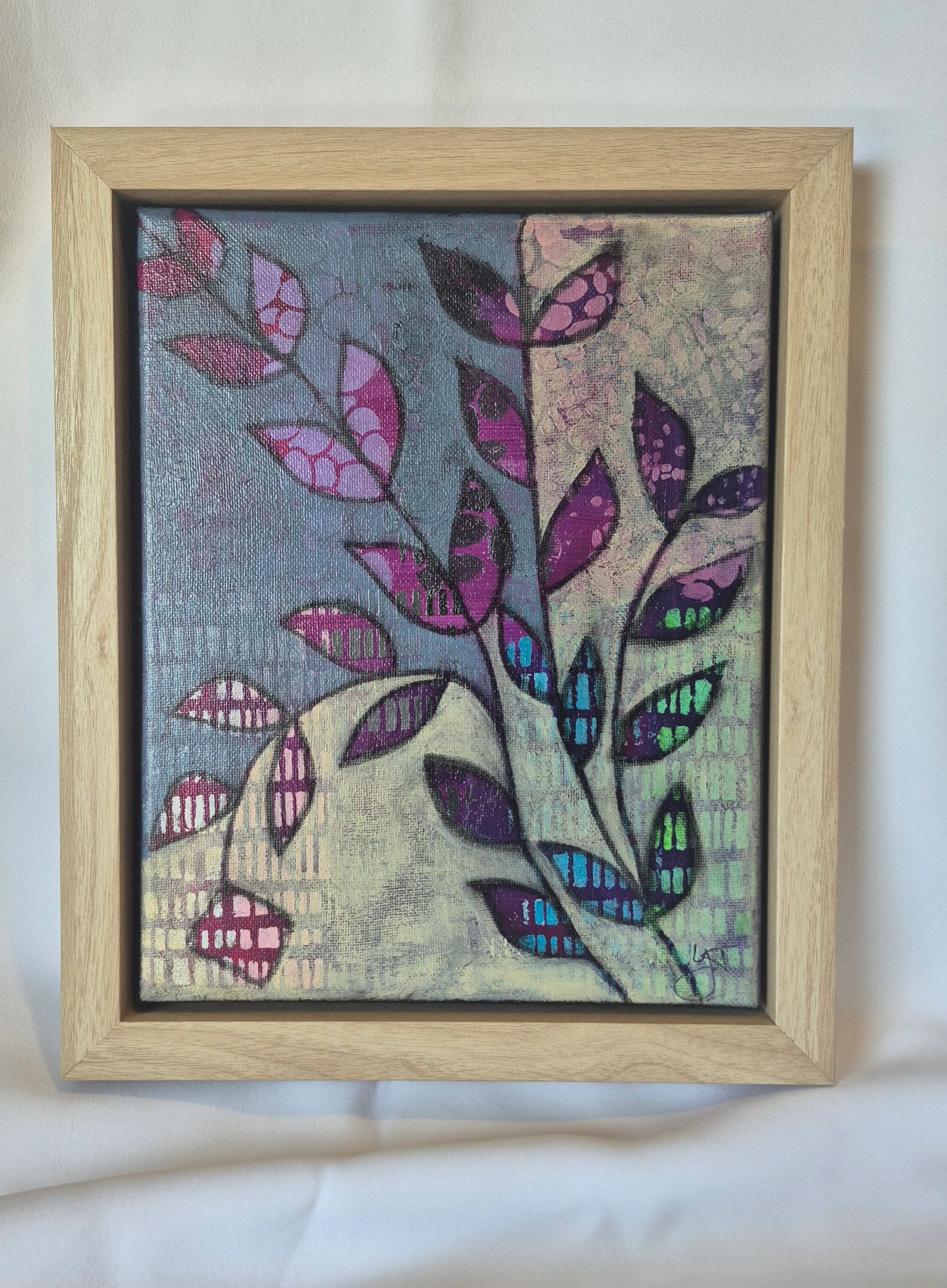 Abstract painting of colorful leaves on canvas in a wooden frame.