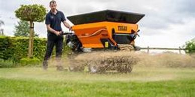 Man operates a large orange lawn spreader on grass.