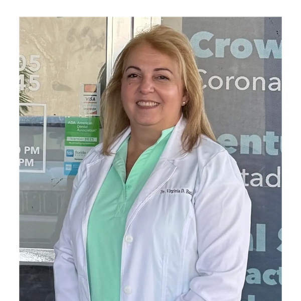 Female doctor smiling, wearing white coat and green scrubs.