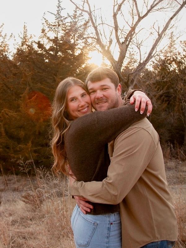 Couple embracing outdoors with warm sunlight and trees in the background.