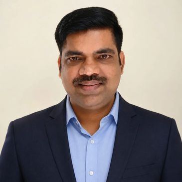 Man in suit with blue shirt posing against a plain background.