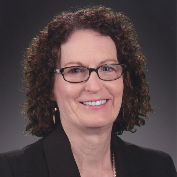 Professional woman with curly hair and glasses smiles warmly.