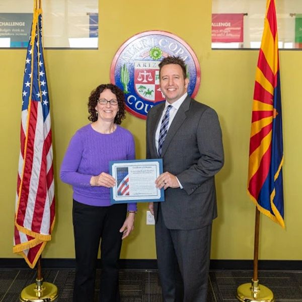Two people holding a certificate between American and Arizona flags.