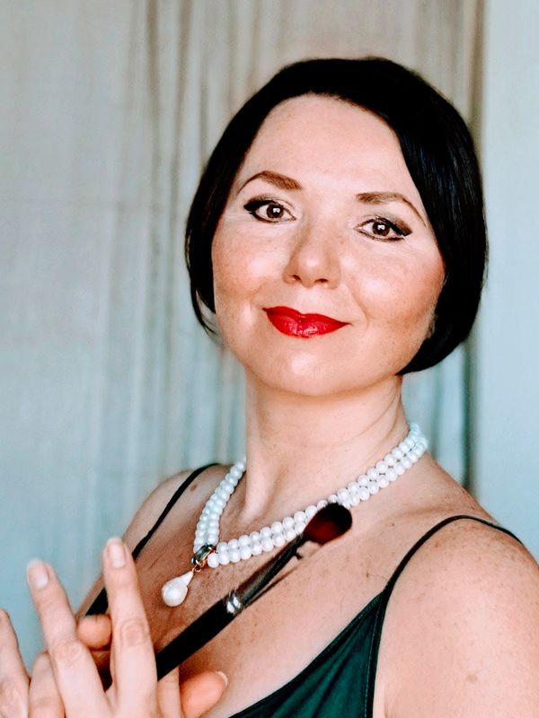 Woman with pearl necklace holding a makeup brush.