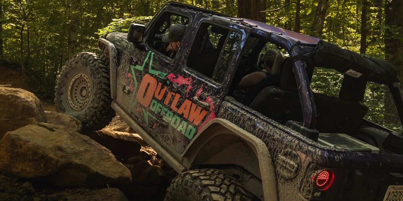 Mud-covered offroad vehicle climbing rocks in a forest.