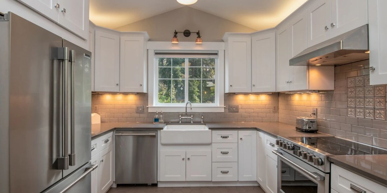 White U-shaped kitchen with farmhouse sink, stainless steel appliances, and tile blacksplash.
