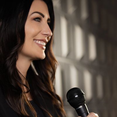 Woman smiling while holding a microphone indoors.