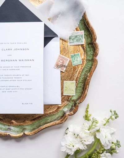Elegant wedding invitation on a vintage tray with stamps and white flowers.