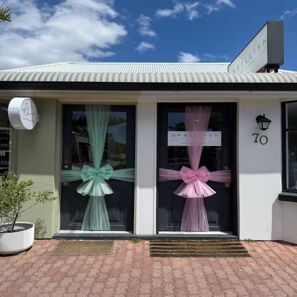 Two black doors decorated with large pastel bows and tulle under a blue sky.
