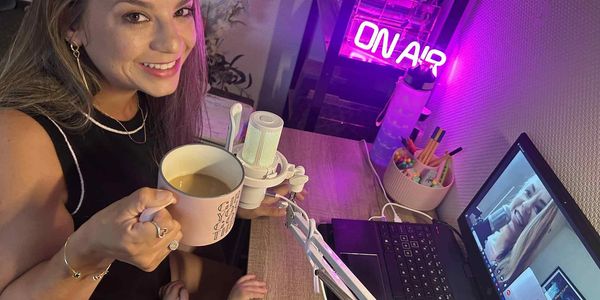 Teresa is enjoying a cup of coffee and smiling during an online recording session while also being a mom.