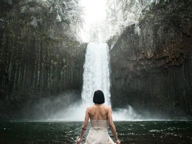 Woman in white dress standing near a majestic snowy waterfall.