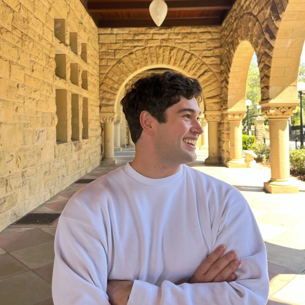 A young man in a white sweatshirt smiling under stone arches.