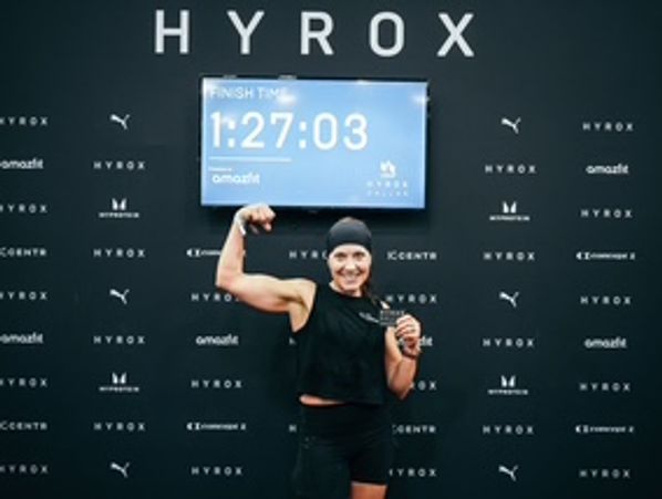 Smiling athlete celebrates finishing HYROX, holding a medal and sign.