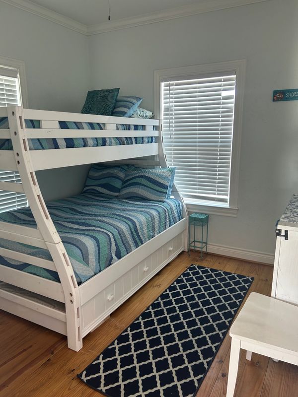 White bunk bed with blue-striped bedding in a bright room with wooden floor.