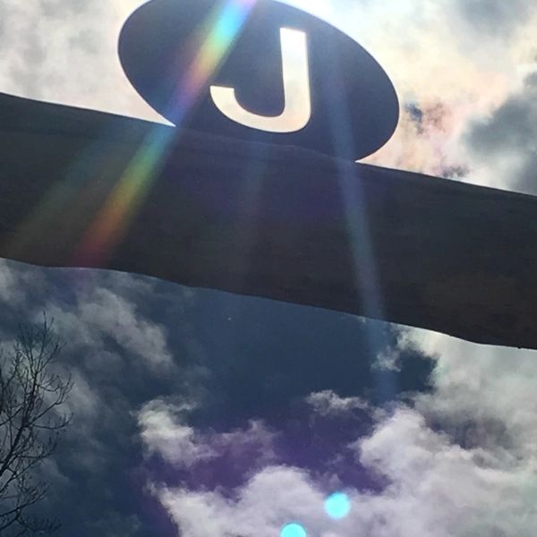A large letter J sign backlit by sun rays and clouds.