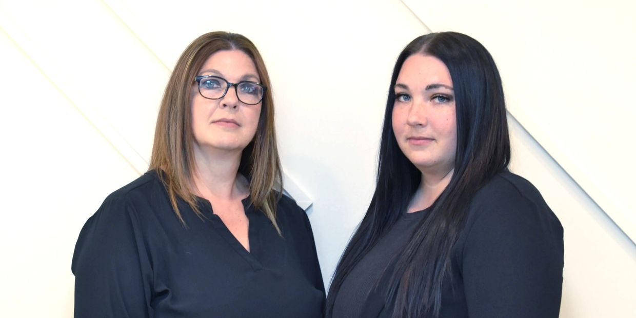 Two women in black tops posing against a white wall.