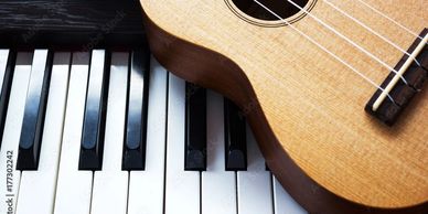 Ukulele resting on piano keys showing contrast of instruments.